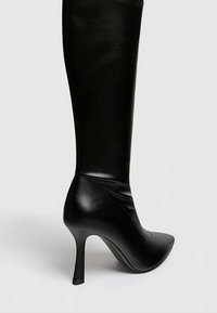 Czarne skórzane wysokie botki z ostro zakończonym noskiem i szpilką. Charakteryzują się gładką fakturą i dopasowanym krojem wzdłuż łydki.