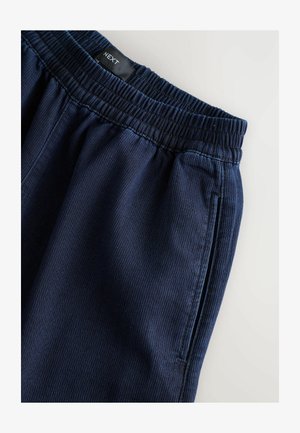 Navy blue, ribbed fabric joggers with an elastic waistband, featuring side pockets and subtle stitching details. Brand label visible.
