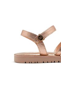 Sandalias metálicas en oro rosa con dos correas finas, un detalle de hebilla redonda y una suela plana de goma con un suelo texturizado para mayor agarre.
