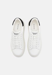 Baskets blanches avec dessus en cuir, lacets blancs et semelle en caoutchouc. Accents noirs au niveau du talon. Logo de la marque sur le côté et la languette.