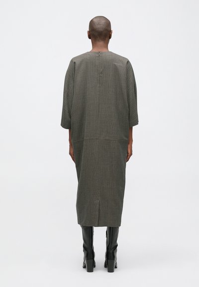 Hosszú, laza szabású szürke ruha finom textúrával, háromnegyedes ujjak, hátsó nyaklezárás és magas hasíték. Fekete térd fölé érő csizmával párosítva.