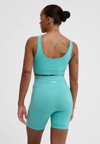 Turkos idrottskorts och matchande shorts i elastiskt material. Har logotyp på midjebandet och ribbat mönster för ökad grepp.