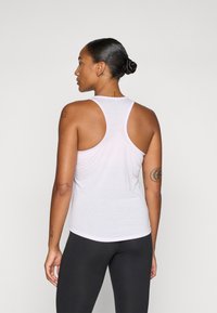 Hvid ærmeløs tanktop med racerback-design, der har en blød tekstur og en afslappet pasform. Kombineret med sorte leggings.