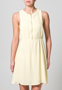 Vestido sin mangas de color amarillo claro con escote redondo, cremallera en el frontal, cintura elástica y tela suave y fluida.