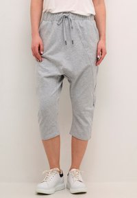 Grå, korte sweatpants med elastisk talje og snor, der har sidelommer og blød tekstur. Båret med hvide sneakers.