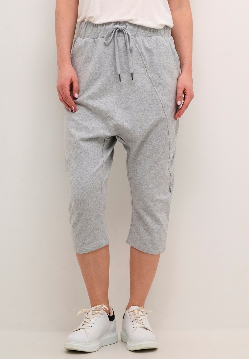 Grå, korte sweatpants med elastisk talje og snor, der har sidelommer og blød tekstur. Båret med hvide sneakers.
