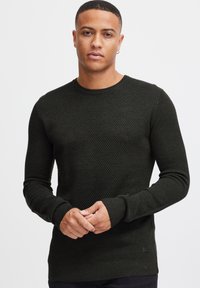 Maglione lavorato a maglia verde scuro con un motivo testurizzato, scollo rotondo, polsini e orlo a costine. Il tessuto appare morbido e leggermente elastico.