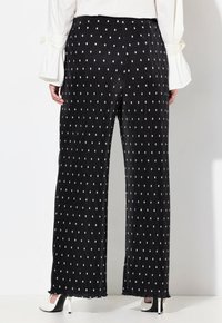 Zwarte wijde broek met witte stippen, met een gemêleerd ribbelontwerp en een verkorte zoom. Het model draagt een witte lange mouwen top.