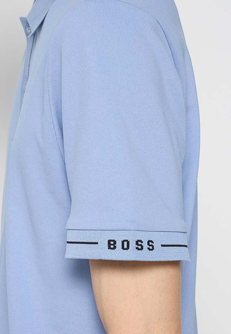 Hellblaues kurzärmliges Poloshirt auf dem Arm, mit "BOSS" in schwarzem Text und horizontalen Linien am Ärmelbund.