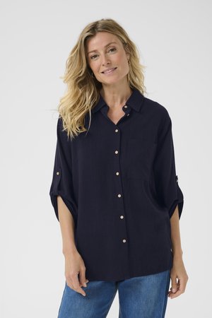 Navy blue button-up shirt with a chest pocket, rolled sleeves, and light brown buttons. Soft texture and relaxed fit.