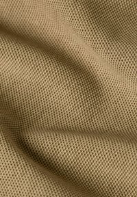 Tessuto beige testurizzato con un motivo a griglia, che presenta un aspetto morbido e intrecciato. Il materiale appare leggero e flessibile.