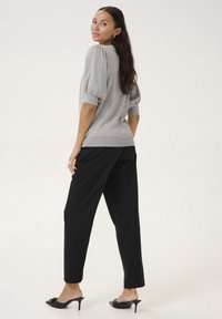 Haut en tricot métallique gris avec des manches bouffantes, associé à un pantalon large noir et des mules à talons noires. Silhouette simple et épurée, au design décontracté.