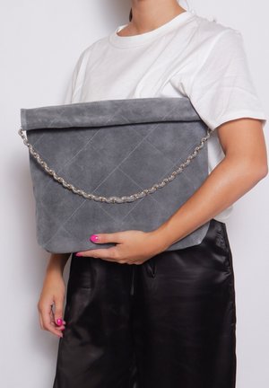 Borsa a busta in suede grigio con motivo trapuntato, accentuata da una catena in argento e design ripiegato, tenuta sotto il braccio.