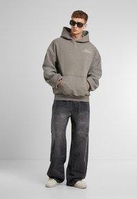 Gray fleece hoodie with a kangaroo pocket, paired with loose black jeans featuring light abstract patterns, and cream sneakers.