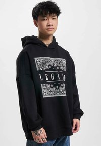 Black oversized hoodie made of cotton, featuring a white paisley pattern and the word "LEGEND" in bold lettering across the front.