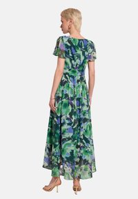 Maxi sukienka z przezroczystego, wielokolorowego materiału z zielonymi i fioletowymi wzorami kwiatowymi, krótkimi rękawami oraz dopasowaną talią, która rozszerza się ku dołowi.