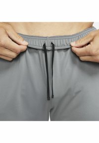 Hände, die den elastischen Bund und die schwarzen Kordeln von grauen Hosen an der Taille und dem unteren Torso einer Person anpassen.