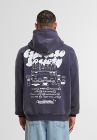Sudadera azul marino con un gran gráfico blanco en la parte posterior que incluye nombres de bebidas de café, íconos y el texto "Another Cotton" en la parte inferior.