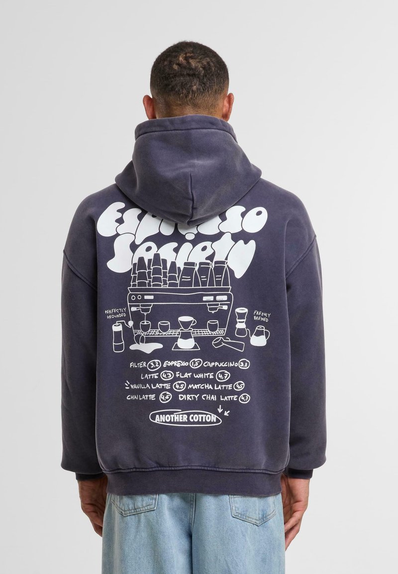 Sudadera azul marino con un gran gráfico blanco en la parte posterior que incluye nombres de bebidas de café, íconos y el texto "Another Cotton" en la parte inferior.