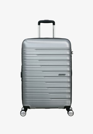 Valigia rigida argento con superficie a righe, maniglia retrattile, quattro ruote e dettaglio logo. Design compatto e leggero.