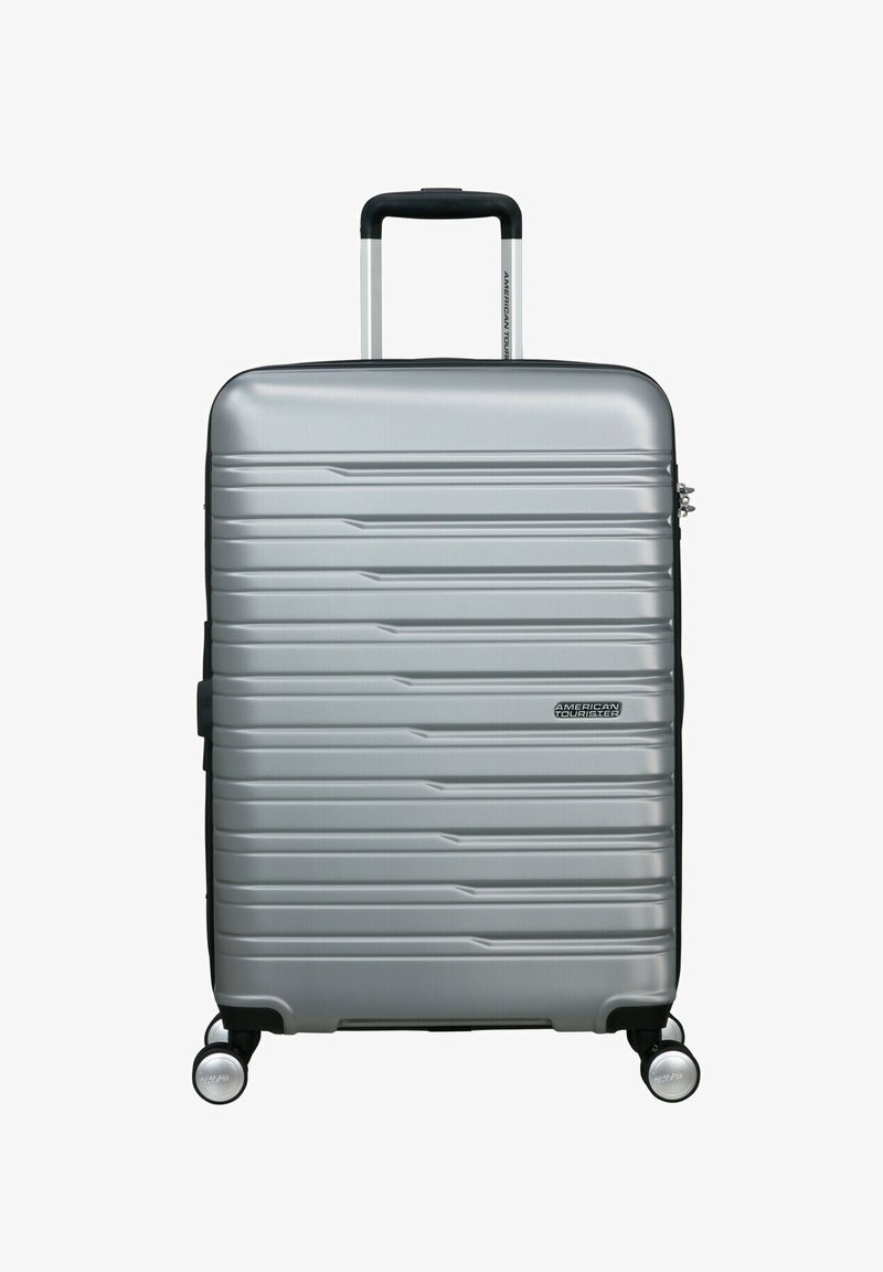 Valigia rigida argento con superficie a righe, maniglia retrattile, quattro ruote e dettaglio logo. Design compatto e leggero.