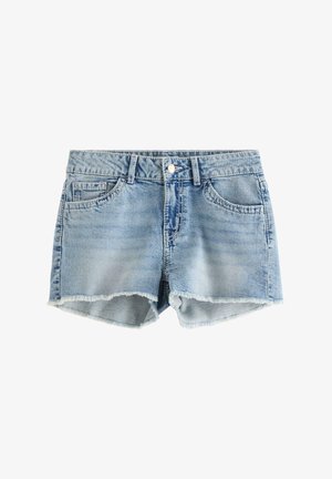 Smilende pige iført en pink flæset en-shoulder top, denimshorts med kædeaccessory og pink platform sneakers på en ensfarvet baggrund.