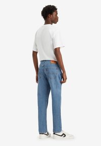 Jeans de denim azul con un corte recto y bolsillos traseros, combinados con una camiseta blanca lisa y zapatillas blancas, mostrando un atuendo casual.