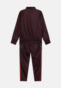 Tuta bordeaux composto da una giacca zippata con colletto alto e pantaloni affusolati. Gli accenti laterali rossi sui pantaloni aggiungono contrasto. Tessuto morbido e elasticizzato.