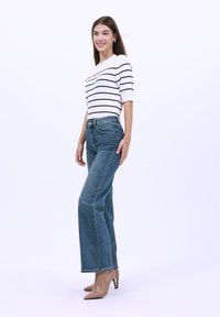 Top a rayas blancas y negras combinado con jeans de pierna recta de tiro alto azules y tacones de aguja nude. Tejido suave y corte ajustado.