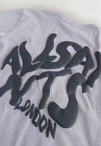 Helehall äri, millel on suur, must, moonutatud tekst, mis moodustab sõnad "ALASAN NYTS LONDON" kangale.