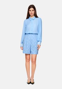 Light blue blouse with buttons and polka dot shorts, both in a soft fabric. Blouse features a collar and patterned cuff details. Black heels.