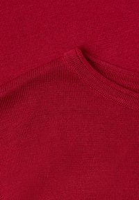 Gros plan d’un tissu tricoté rouge montrant un col plié avec des coutures fines et un motif de trame texturé.