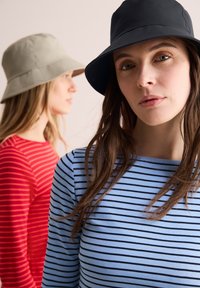 Due donne con cappelli a secchiello e magliette a righe. Una indossa un cappello blu scuro e una maglietta a righe blu; l'altra ha un cappello beige e una maglietta a righe rosse.