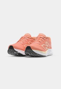 Des chaussures de course légères en maille corail et pêche avec des accents réfléchissants. Elles disposent d'une semelle rembourrée et d'une semelle extérieure en caoutchouc noir texturé.