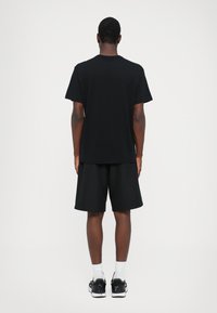 Svart bomull t-skjorte med korte ermer, kombinert med svarte shorts. Outfitten fullføres med hvite sokker og svarte joggesko.