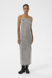Vestido maxi de ganga cinza sem alças, com costuras verticais e uma textura subtil. Modelo usa botas plataforma pretas. Design simples e minimalista.