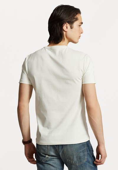 Kort hvit bomull T-skjorte med rund hals og korte ermer, båret av en person som vender bort, kombinert med blå jeans.
