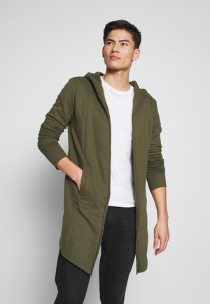 Olivegrøn lang hoodie med lynlås foran, sidelommer og en afslappet pasform. Fremstillet af blødt materiale med en glat tekstur.