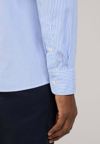 Camicia a righe blu chiaro con maniche a polsino classiche, texture morbida e vestibilità su misura, con bottoni bianchi e righe a contrasto.