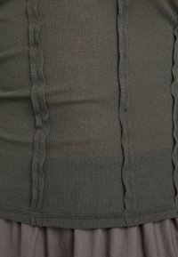 Dark green ribbed top featuring vertical seams and a fitted design. The fabric is slightly sheer with a smooth texture and subtle sheen.