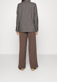 Blazer à carreaux marron avec une coupe ajustée, associé à un pantalon large marron fluide, mettant en valeur des boutons élégants et un dos épuré.