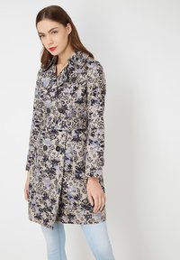 Trench coat con estampado floral en beige, azul y negro. Cuenta con un amplio cuello, mangas largas, cinturón y botones de doble botonadura.