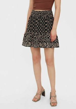 Sort nederdel med blomsterprint i creme. Har en flæset kant og elastisk talje. Glat stof. Båret med strappy, højhælede sandaler.