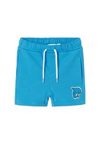 Blaue Shorts aus weichem Stoff, mit einem elastischen Bund und weißem Kordelzug, sowie einer Haifisch-Applikation auf der linken Seite.