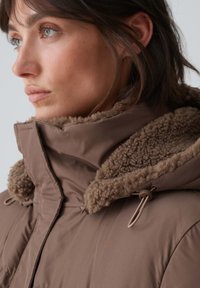Brown insulated jacket with a soft, fuzzy collar and adjustable hardware. Features a smooth exterior and a warm interior texture.