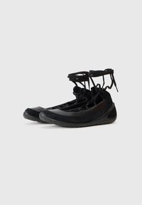 Des chaussures de sport noires combinant des matériaux mats et brillants, dotées d'une forme flexible et d'un système de laçage complexe pour un ajustement sécurisé.