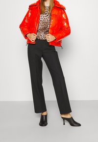 Doudoune rouge à finition brillante, fermeture zippée, haut noir à imprimé animal, pantalon noir sur mesure, mules noires à talons.