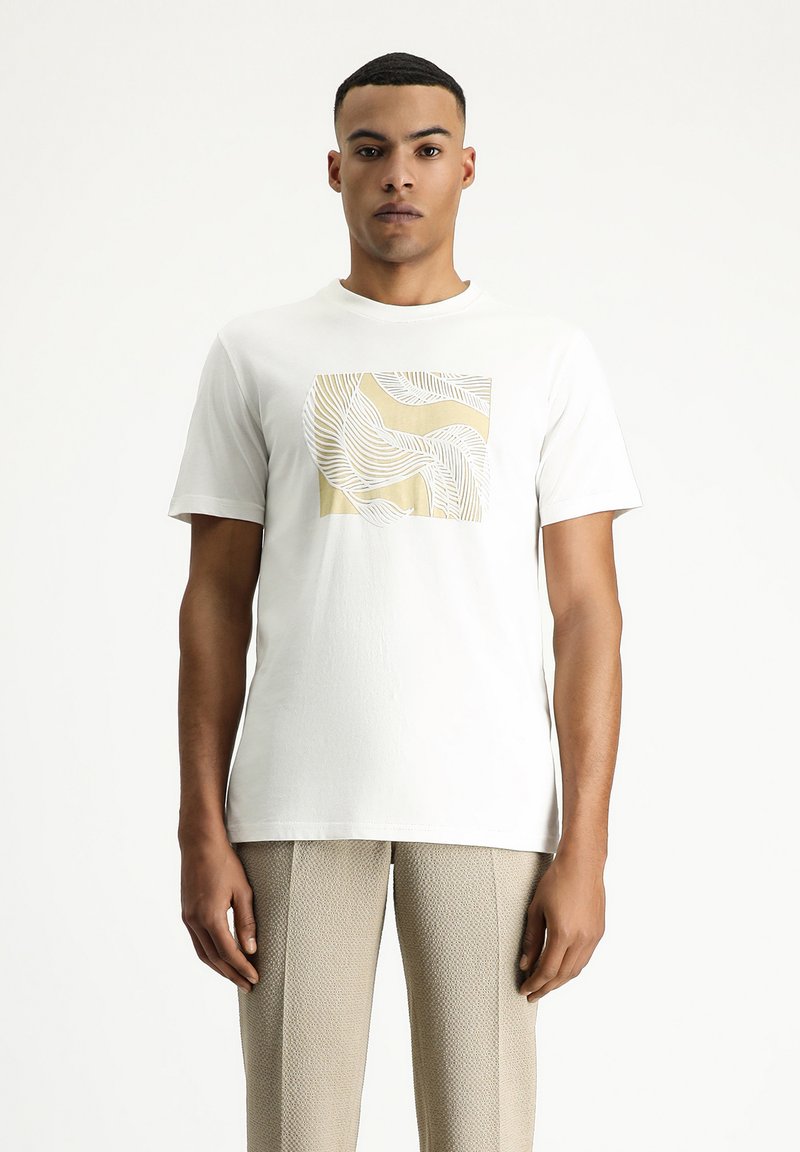 Camiseta de algodón blanca con un gráfico cuadrado en dorado claro y líneas blancas onduladas. Textura suave y corte relajado. Fondo neutro.