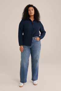 Camisa de botones de manga larga de color marino combinada con jeans de pierna ancha en azul claro. Tejido suave, diseño con cuello y zapatillas deportivas casuales.