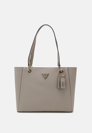 Sac cabas beige Guess avec double poignées, surface texturée, triangle logo en métal et deux étiquettes suspendues marquées Guess et 1981.
